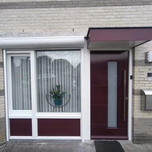 Moderne bordeauxrode voordeur met luifel en witte kozijnen